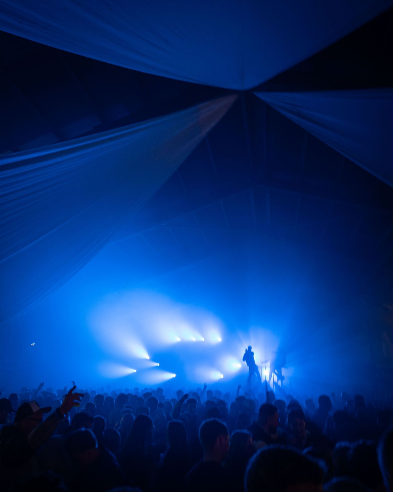 Blau leuchtende Bühne in der Scheune mit an der Decke hängenden Segeln. – Maifeuerfete Fehmarn 2026