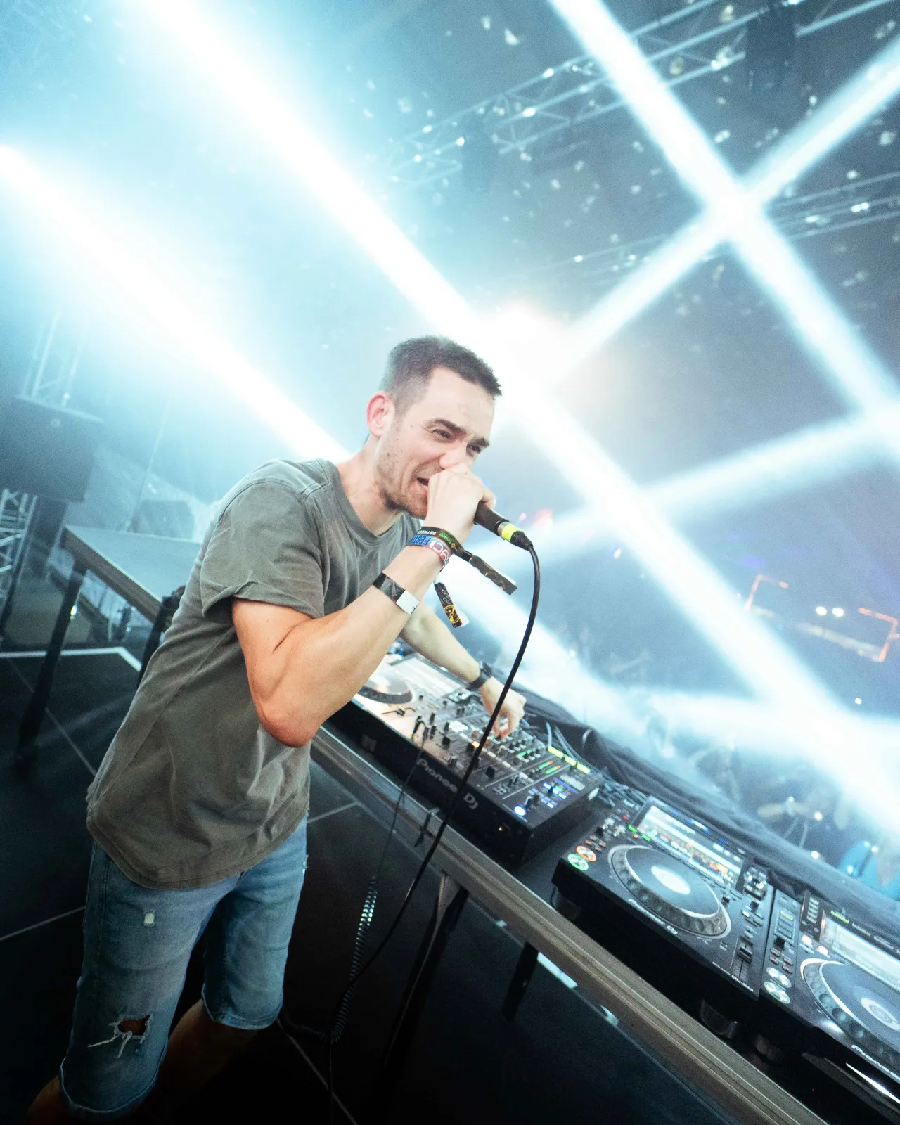 Special D am DJ Pult mit Mikrofon in der Hand und Lichtstrahlen im Hintergrund