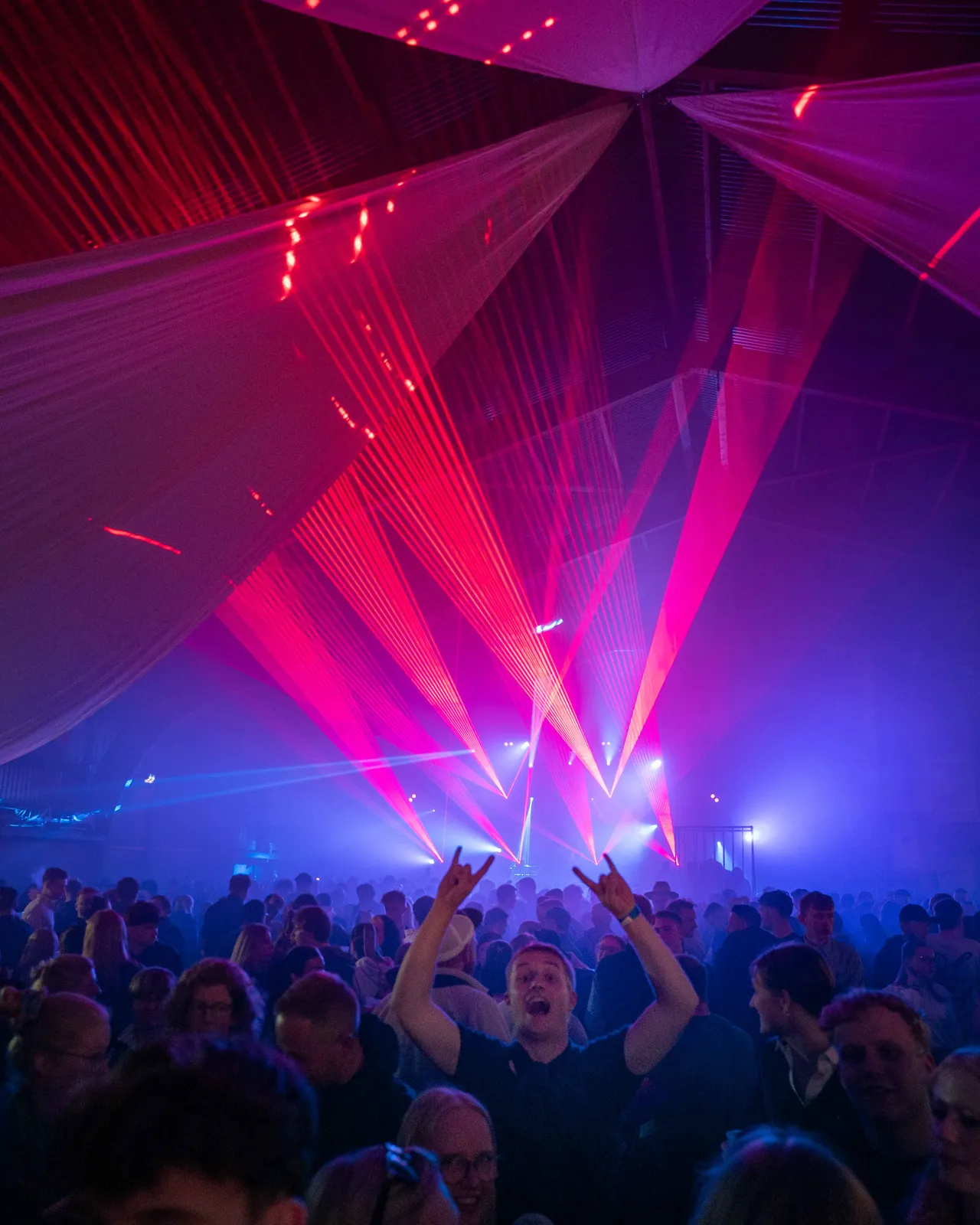 Blaues Licht und rote Laser von der Bühne. Ein Gast reißt Hände in der Crowd hoch.