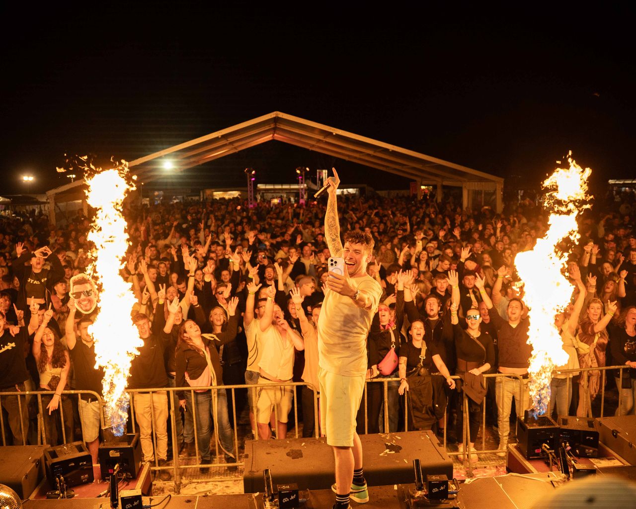 LeShuuk steht auf Bässen. Crowd reißt Hände hoch. Flammen schießen links und rechts in die Höhe.