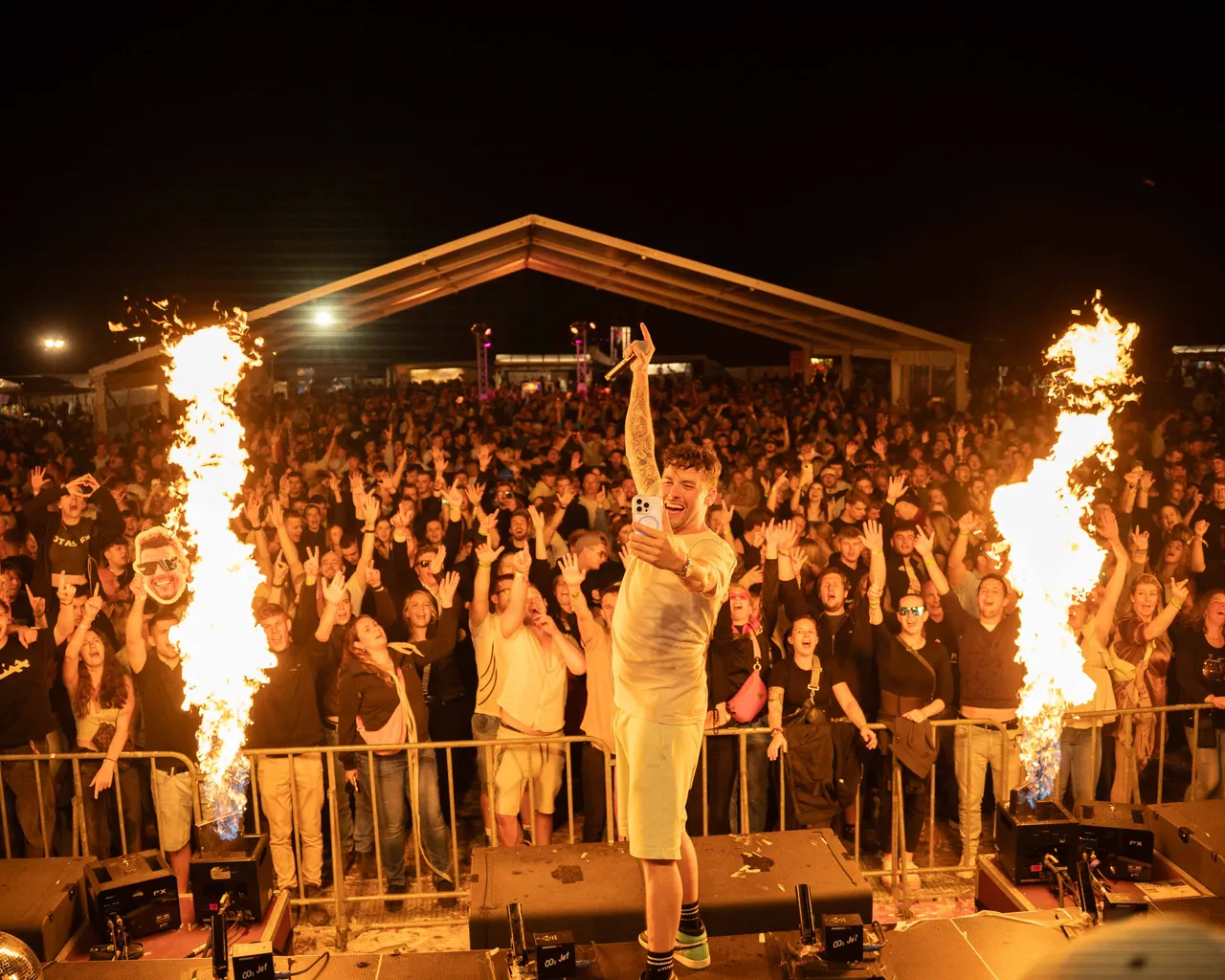 LeShuuk steht auf Bässen. Crowd reißt Hände hoch. Flammen schießen links und rechts in die Höhe.