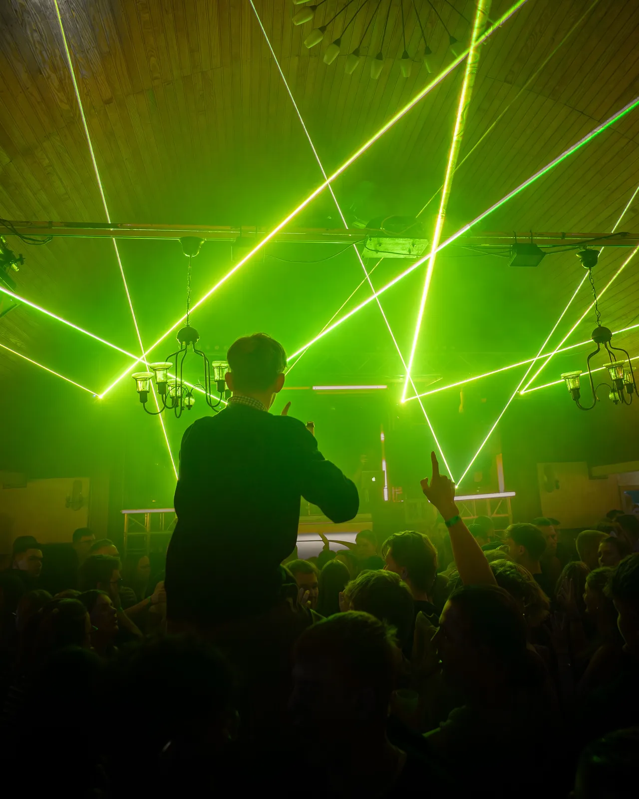 Gast auf den Schultern eines anderen. Im Hintergrund kommen grüne Laserstrahlen von der Bühne.
