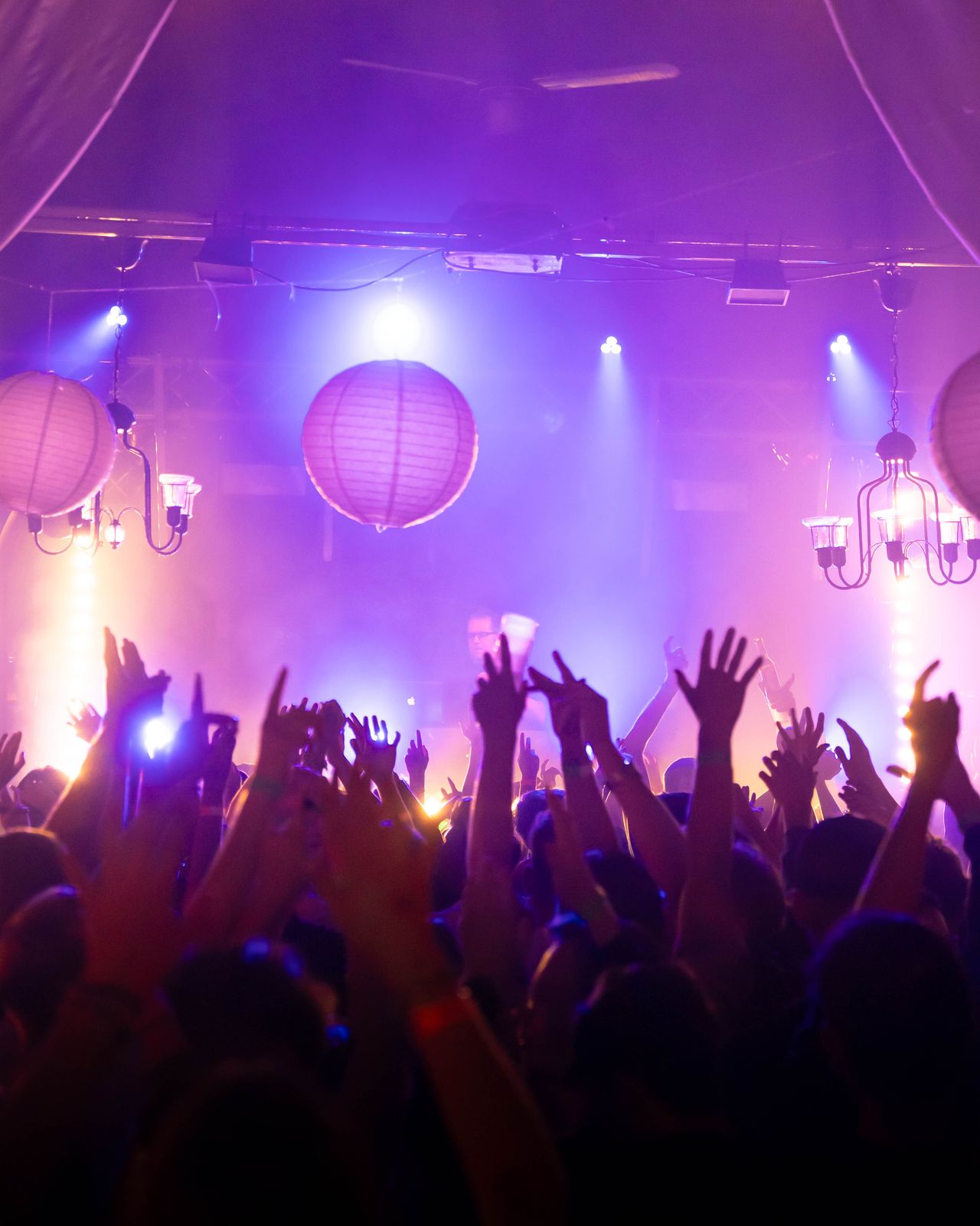 Crowd reißt Hände im lila orangenem Licht hoch.