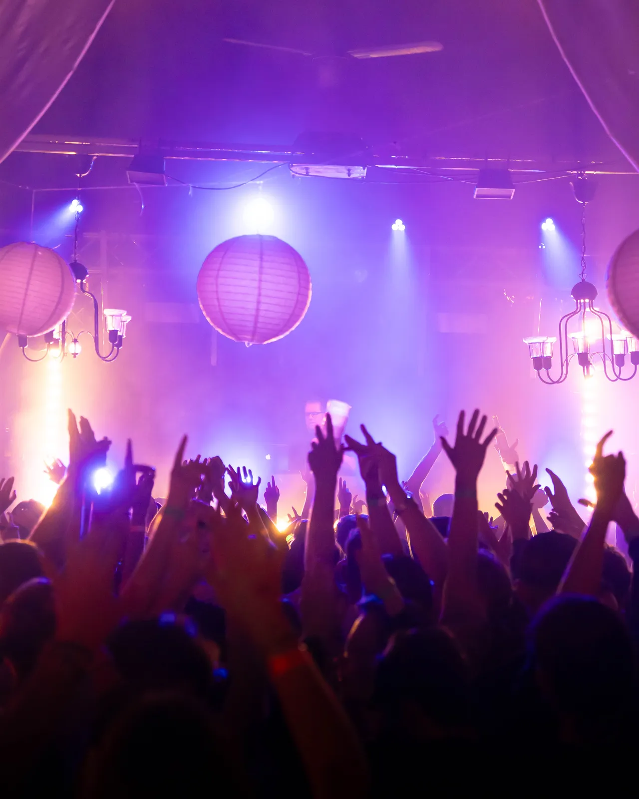 Crowd reißt Hände im lila orangenem Licht hoch.